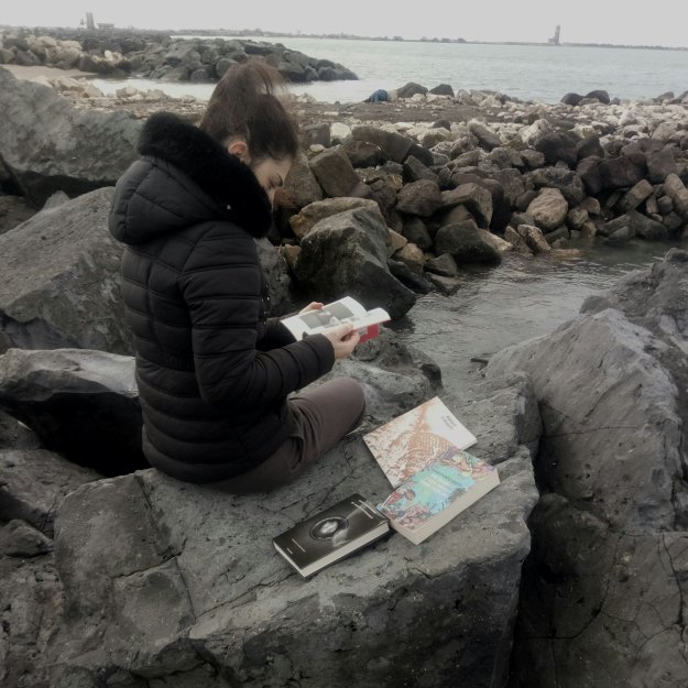 Nel calduccio del suo studiolo, Ilaria Petrarca sfoglia i libri ricevuti in premio per il gioco-concorso "Fermo-paesaggio"